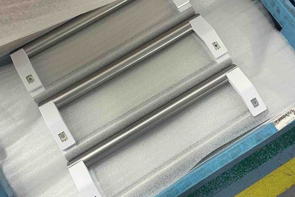 Three tubular metal handles with white end mounts lie side-by-side on protective foam padding inside a transport crate.